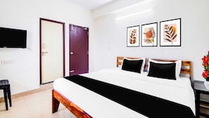 A hotel room with a bed, a TV, a door, and three framed artworks on the wall. - Collection Rushikonda Beach Near GITAM (Visakhapatnam)