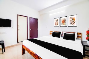 Ein Hotelzimmer mit Bett, Fernseher, Tür und drei gerahmten Kunstwerken an der Wand.