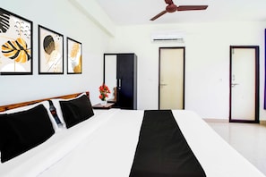 Ein Hotelzimmer mit Bett, Kleiderschrank, Tür, Klimaanlage und gerahmten Kunstwerken an der Wand.