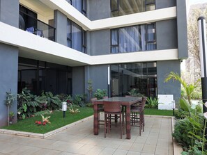 A modern building with a courtyard featuring a dining area with wicker furniture. - Modern 1-Bedroom near Sarit Centre Mall, Museum, City attractions & Top Dining (Nairobi)