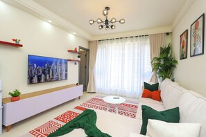 A modern living room with a flat-screen TV, a white sofa, patterned rugs, and a ceiling light fixture. - Modern 1-Bedroom near Sarit Centre Mall, Museum, City attractions & Top Dining (Nairobi)