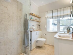 Un baño con cabina de ducha de vidrio, inodoro, lavabo con tocador y ventana con vistas.