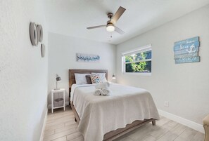 A bedroom with a bed, a ceiling fan, a window with a view, and a wall with a decorative sign. - Fenced Backyard 2BR Pet Friendly and Sleeps 6 (Clearwater)