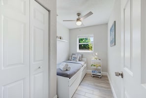 A narrow hallway leading to a bedroom with a bed, a window, a ceiling fan, and a small shelf with items. - Fenced Backyard 2BR Pet Friendly and Sleeps 6 (Clearwater)