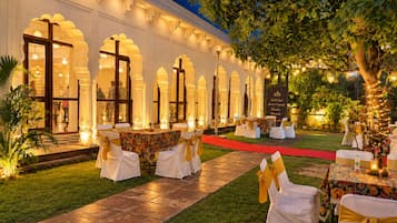 An outdoor event space with tables and chairs, a red carpet, and a building with arched windows.