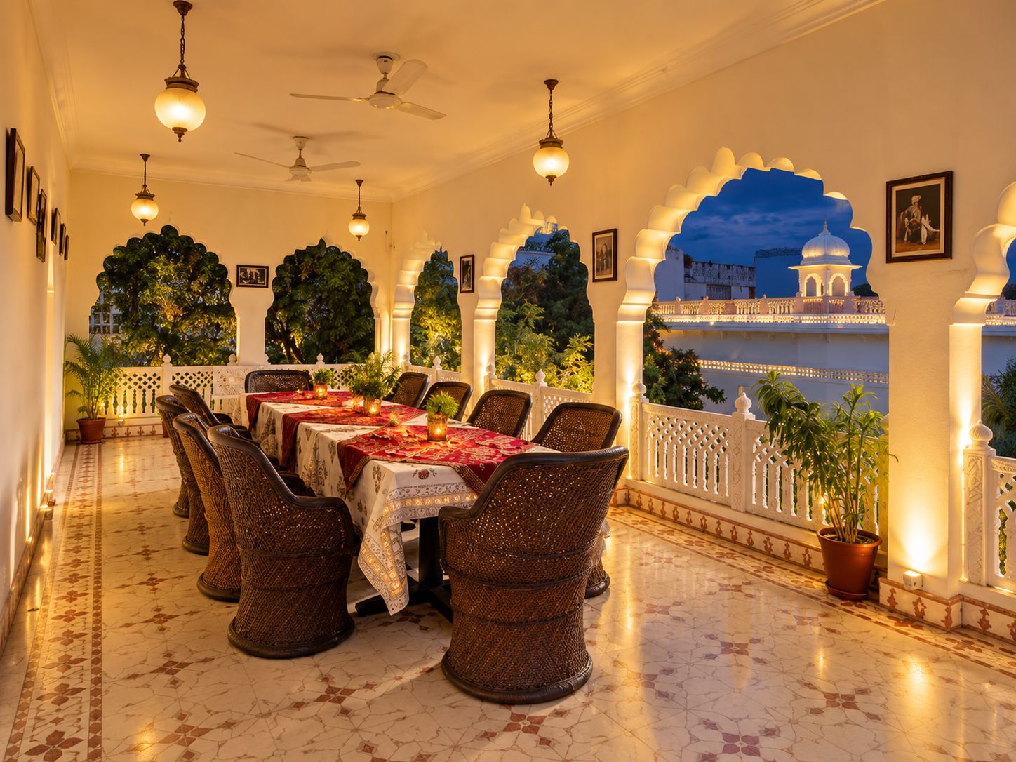 Comedor con vista a un palacio, mesas dispuestas con manteles, sillas de mimbre y plantas en macetas.