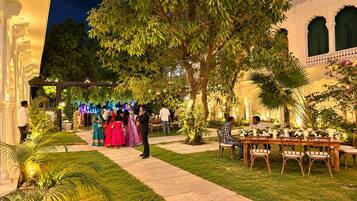 An outdoor dining area with a table set for two, surrounded by greenery and a building with traditional architecture.