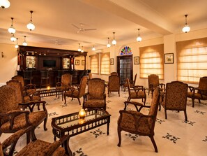 A bar area with a television, bar stools, and a patterned floor. There are multiple chairs arranged around a central table with a vase.