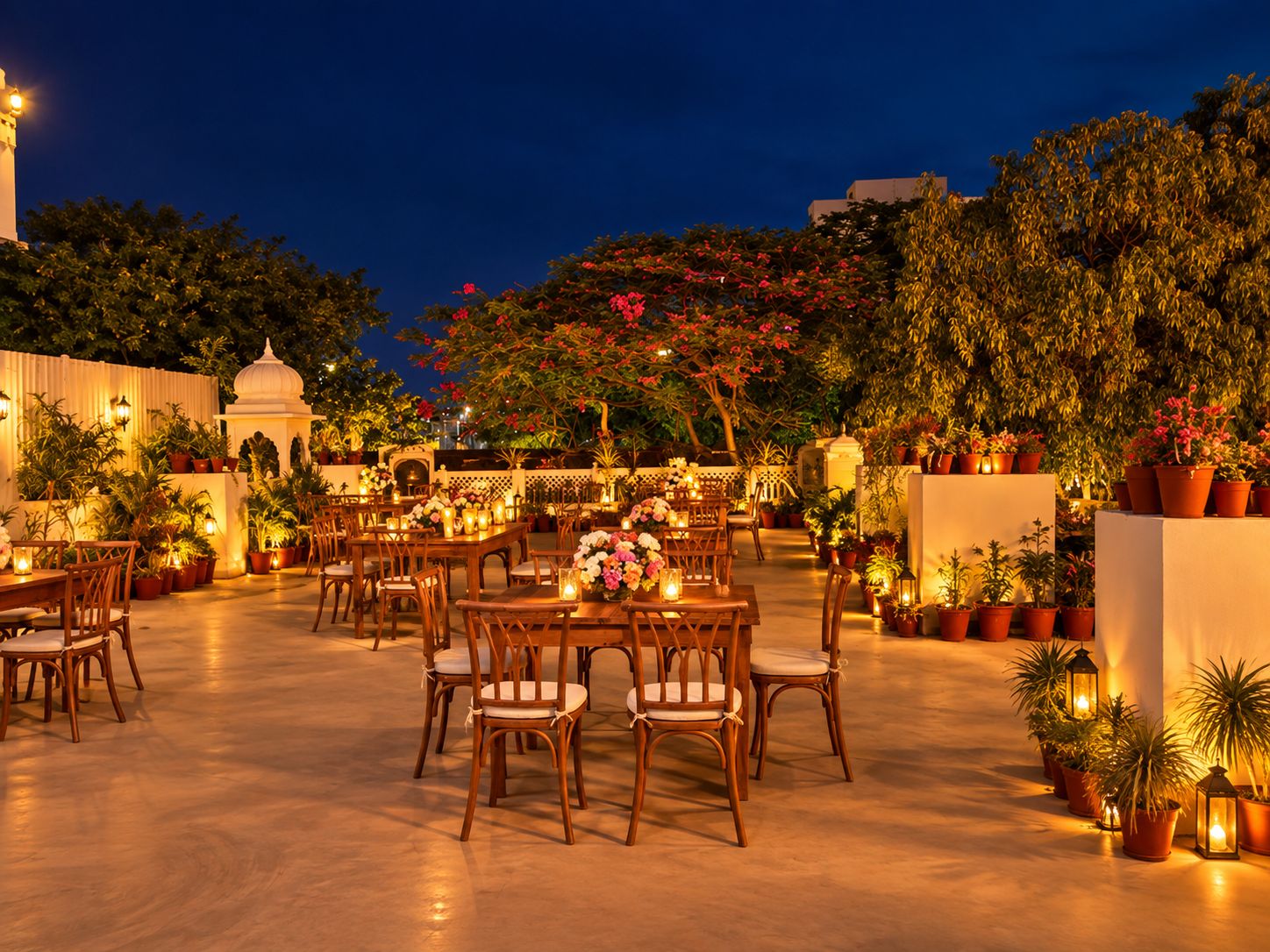 An outdoor dining area with tables and chairs, surrounded by potted plants and a white building with a dome structure.