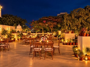 An outdoor dining area with tables and chairs, surrounded by potted plants and a white building with a dome structure. - Khandwa Haveli – A Boutique Heritage Hotel, Jaipur (Jaipur)
