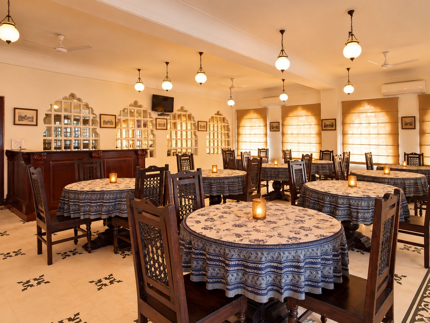 A restaurant with round tables, chairs, hanging light fixtures, and decorative wall sconces.