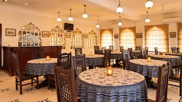A restaurant with round tables, chairs, hanging light fixtures, and decorative wall sconces.