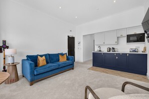 A modern living room with a blue sofa and a kitchen with white cabinets and a dark blue island. - Seaview Largs - 1 Bedroom Ground Floor Apartment (Largs)