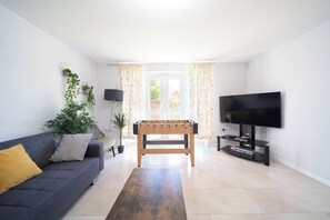 Un saló amb un sofà, una taula de futbolí, una televisió i una finestra amb cortines.