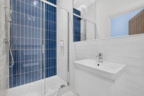 A bathroom with a glass-enclosed shower, a white sink, and a mirror above the sink. - Seaview Largs - 1 Bedroom Ground Floor Apartment (Largs)