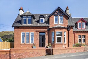 A two-story house with a brick facade, multiple windows, and a prominent front entrance. - Seaview Largs - 1 Bedroom Ground Floor Apartment (Largs)