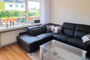 Ein modernes Wohnzimmer mit einem Ecksofa, einem Glastisch und Blick ins Freie.