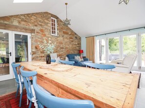 A dining area with a wooden table, blue chairs, and a stone wall. - The Homestead (Newquay)