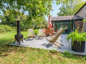 An outdoor patio with a wood-burning stove, wooden chairs, and a table. - The Homestead (Newquay)