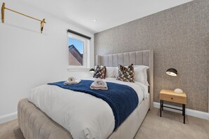 Een moderne slaapkamer met een groot bed, een nachtkastje met lamp en een raam met uitzicht.