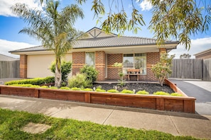 A residential house with a tiled roof, brick exterior, and a front yard with a wooden planter and various shrubs.