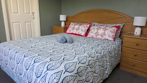 A neatly made bed with a leaf-patterned duvet, two bedside lamps, and a wooden headboard.