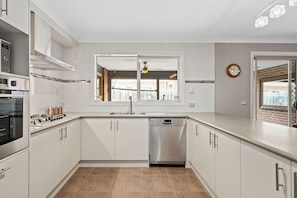A modern kitchen with white cabinetry, a dishwasher, and a window with a view of the outside.