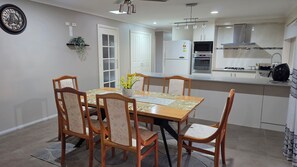 Cozinha moderna com área de refeições, destacando uma mesa de madeira, cadeiras e um relógio na parede.