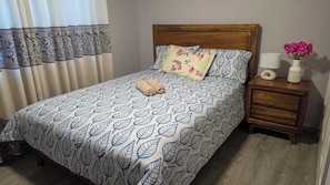 A neatly made bed with a leaf-patterned bedspread, a wooden headboard, and a bedside table with a vase of flowers.