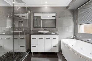 A modern bathroom with a glass shower enclosure, a freestanding bathtub, and a vanity with a large mirror.