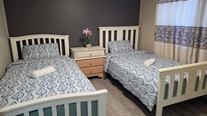 Quarto com duas camas de solteiro, mesa de cabeceira, cômoda e janela com cortinas.