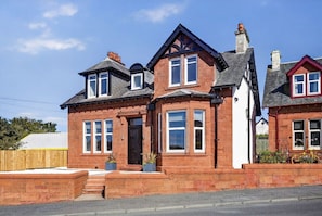 A two-story brick house with a gabled roof, a front porch, and a small garden area. - Seaview Largs - 2 Bedroom Apartment (Largs)