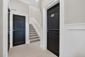 A hallway with two dark doors, a carpeted staircase, and white trim. - Seaview Largs - 2 Bedroom Apartment (Largs)