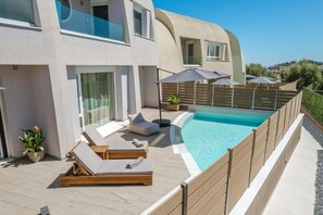 Eine moderne Villa mit Swimmingpool, Liegestühlen und einer überdachten Sitzgruppe.