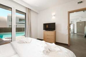 Ein Hotelzimmer mit Bett, Fernseher auf einer Holzkommode, einem großen Fenster mit Blick auf einen Swimmingpool und einer Tür zu einem weiteren Raum.
