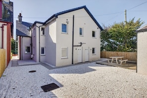 A two-story house with a gravel driveway, a wooden fence, and a picnic table in the backyard. - Seaview Largs - 1 Bedroom Apartment (Largs)