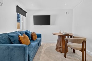 A modern living room with a blue sofa, a round wooden table, and a single chair. - Seaview Largs - 1 Bedroom Apartment (Largs)