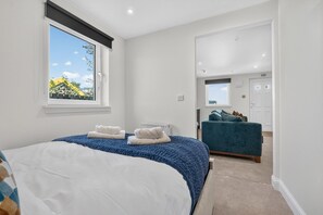 Ein Schlafzimmer mit einem großen Bett, einem Fenster mit Ausblick, einem blauen Sessel und einer Tür zu einem anderen Raum.