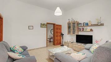 Una sala de estar con sofá, mesa de centro, televisor y estantería.