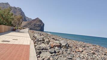 A paved walkway beside a rocky shoreline with a mountain in the background.