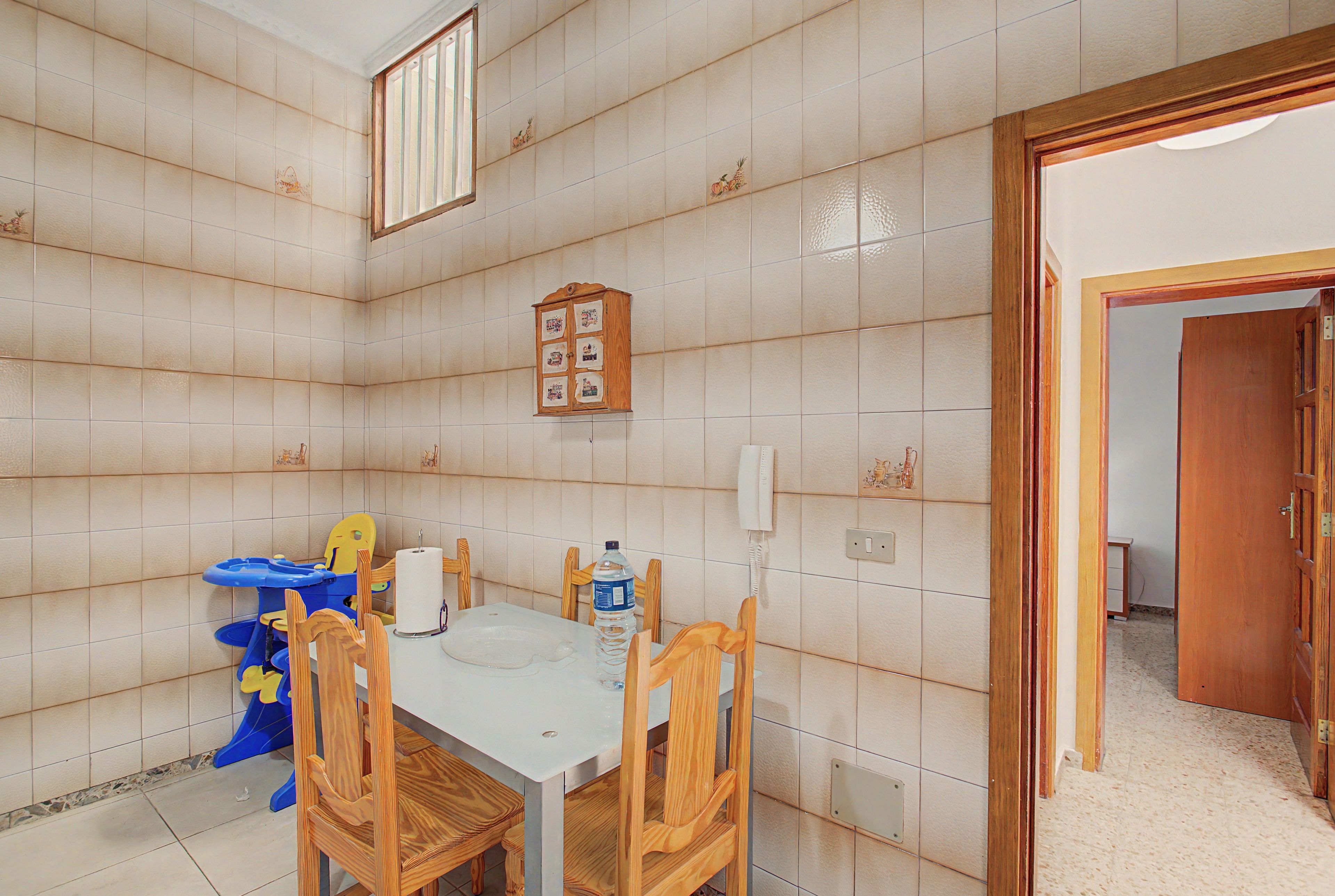 A room with a tiled wall, a wooden cabinet with pictures, a table with chairs, and a blue and yellow toy.