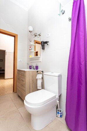 Une salle de bain moderne avec des toilettes blanches, un meuble-lavabo en bois, un miroir et un rideau de douche violet.