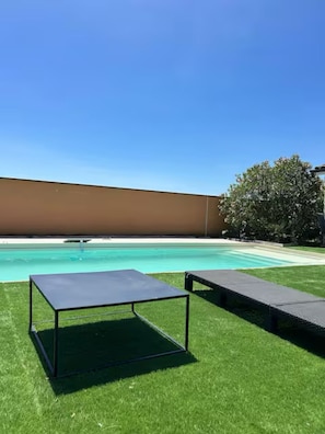 A swimming pool with a clear blue sky, a grassy area, and two lounge chairs.