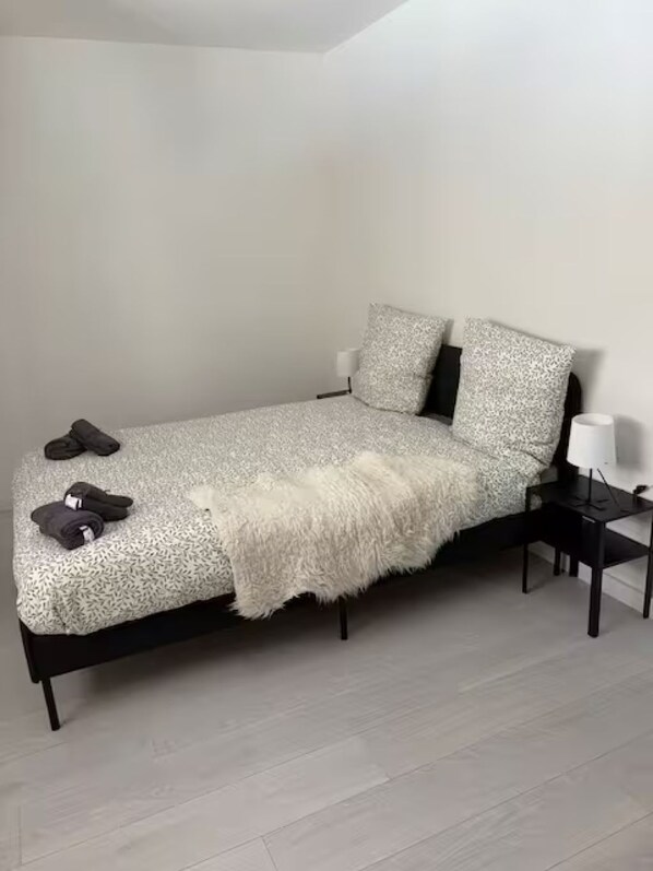 A bed with a patterned bedspread, a fluffy throw blanket, and two pillows. There are two bedside tables with lamps.