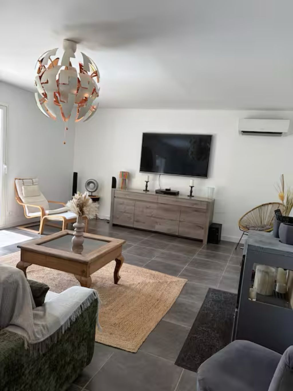 Een moderne woonkamer met een grote flatscreen televisie, een houten salontafel, een beige vloerkleed en een bijzondere bolvormige kroonluchter.