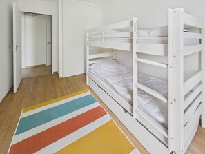 Ett rum med en våningssäng, en dörr som leder till en garderob och en färgglad, randig matta.