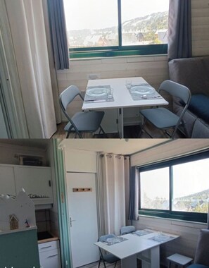 A compact room with a table set for two, a small kitchenette, and a view of a mountainous landscape through large windows. - Cozy studio apartment 50 meters from the base of the slopes (Arette la Pierre saint)