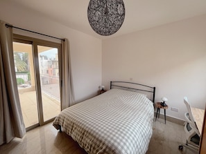 A bedroom with a bed, a nightstand, a chair, a table, and a balcony with curtains. - Spacious 5-bedroom house with AC in lovely Poli Chrysochous (Poli Chrysochous)