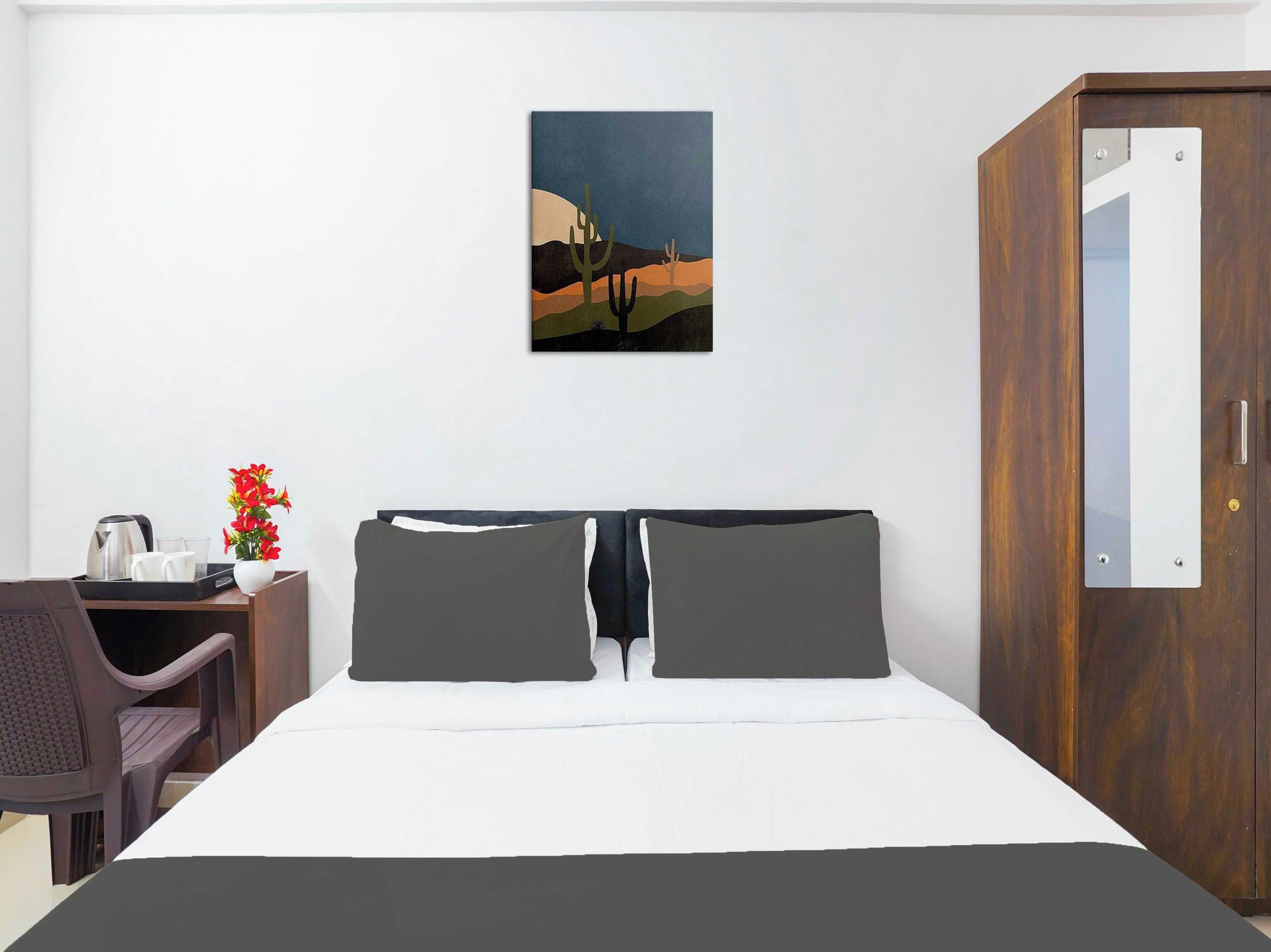 Ett hotellrum med en säng, ett skrivbord med en stol, en vas med blommor och en tavla på väggen.