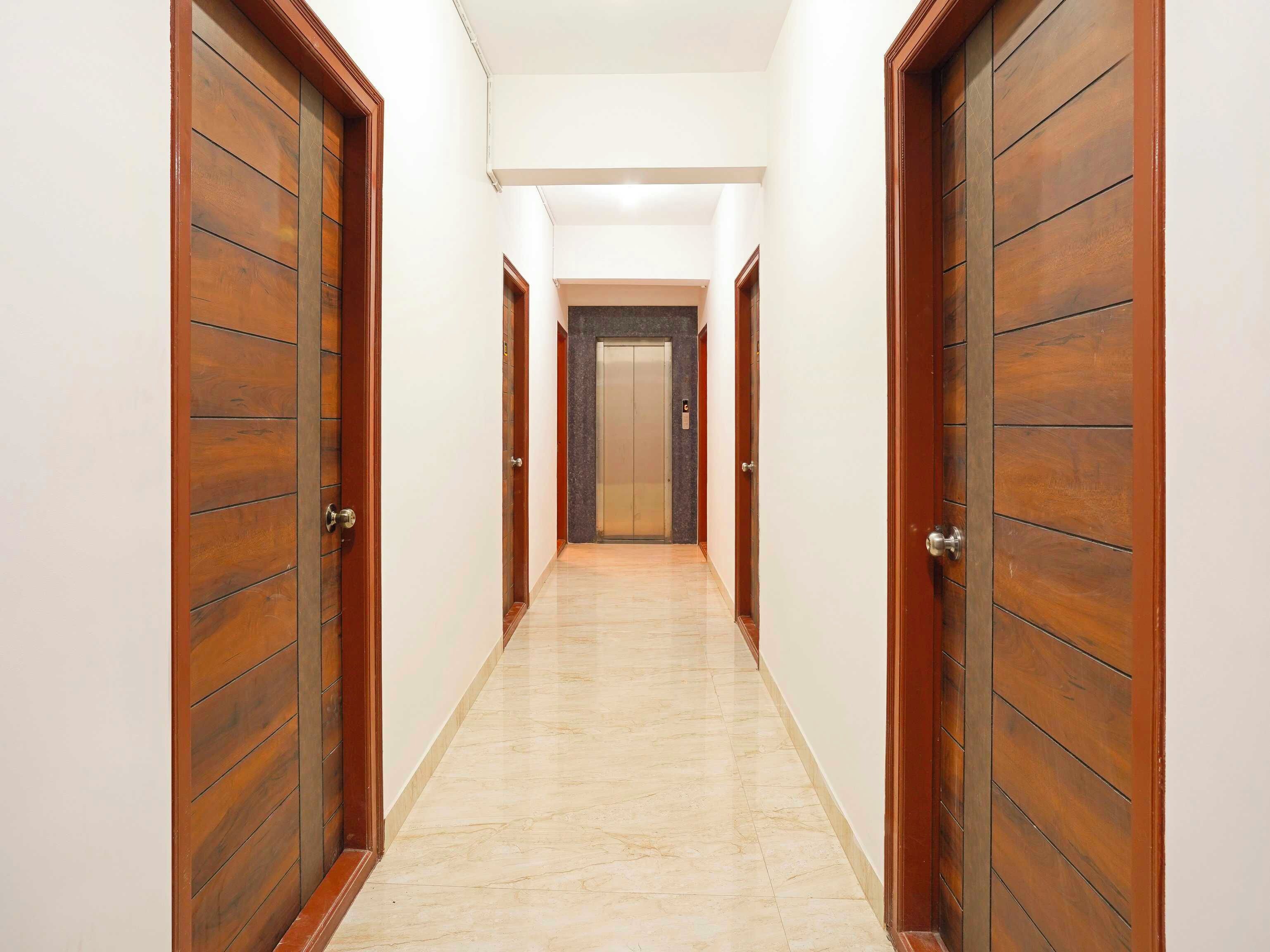 A corridor with wooden doors and a marble floor, leading to an elevator.
